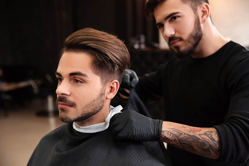 A handsome young man having his hair trimmed and styled by a professional barber