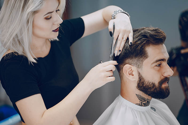 A handsome young man having his hair trimmed by a professional female barber