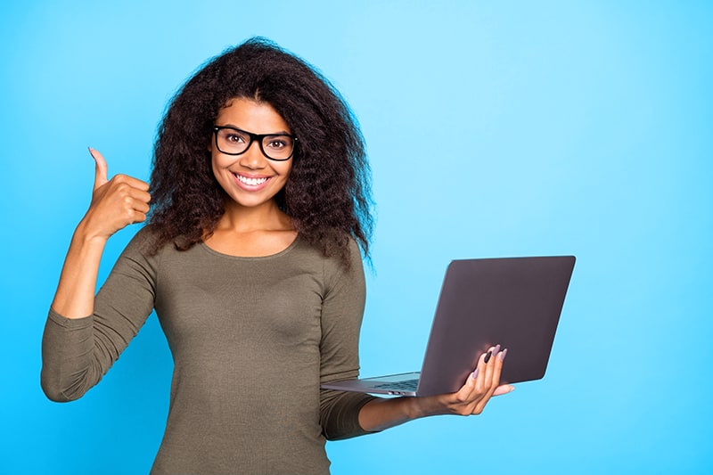 A confident young woman holding a laptop and smiling
